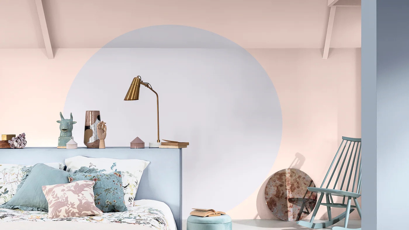 Quarto decorado com uma pintura em círculo na cor Portal Secreto da Tintas Coral. A mistura de rosa, lilás e azul deixou o ambiente agradável e relaxante, além de um toque moderno dados pelos objetos de decoração presentes no quarto.   