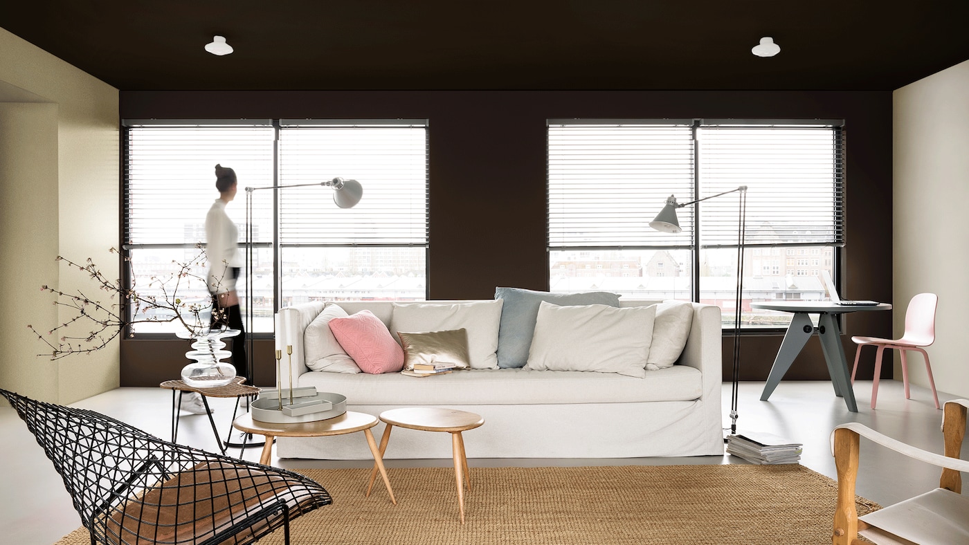 Sala com paredes decoradas e uma mulher olhando pela janela de vidro.