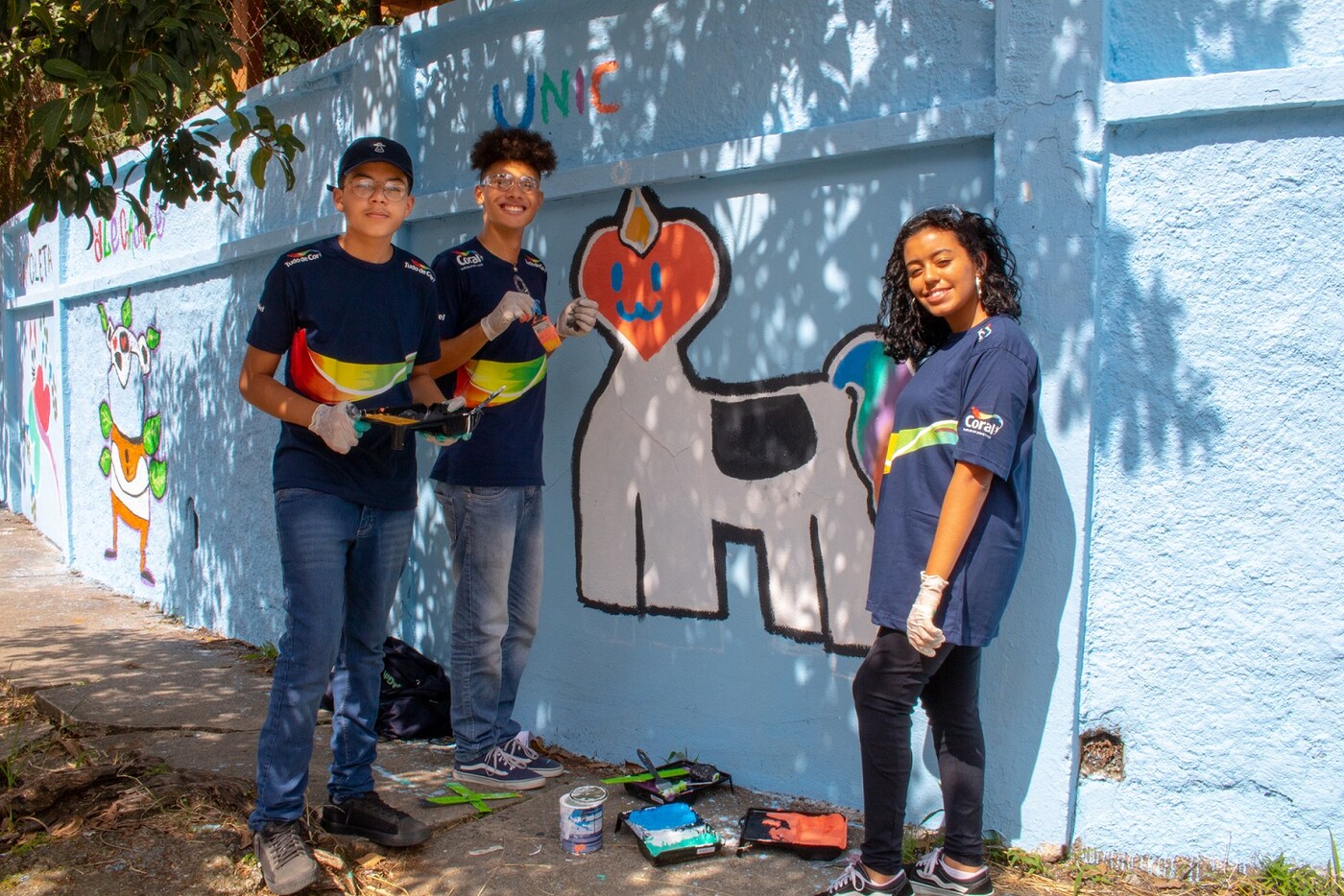 Três pessoas pintando um muro no projeto ImaginaC em total sintonia com programa Tudo de Cor da Coral.
