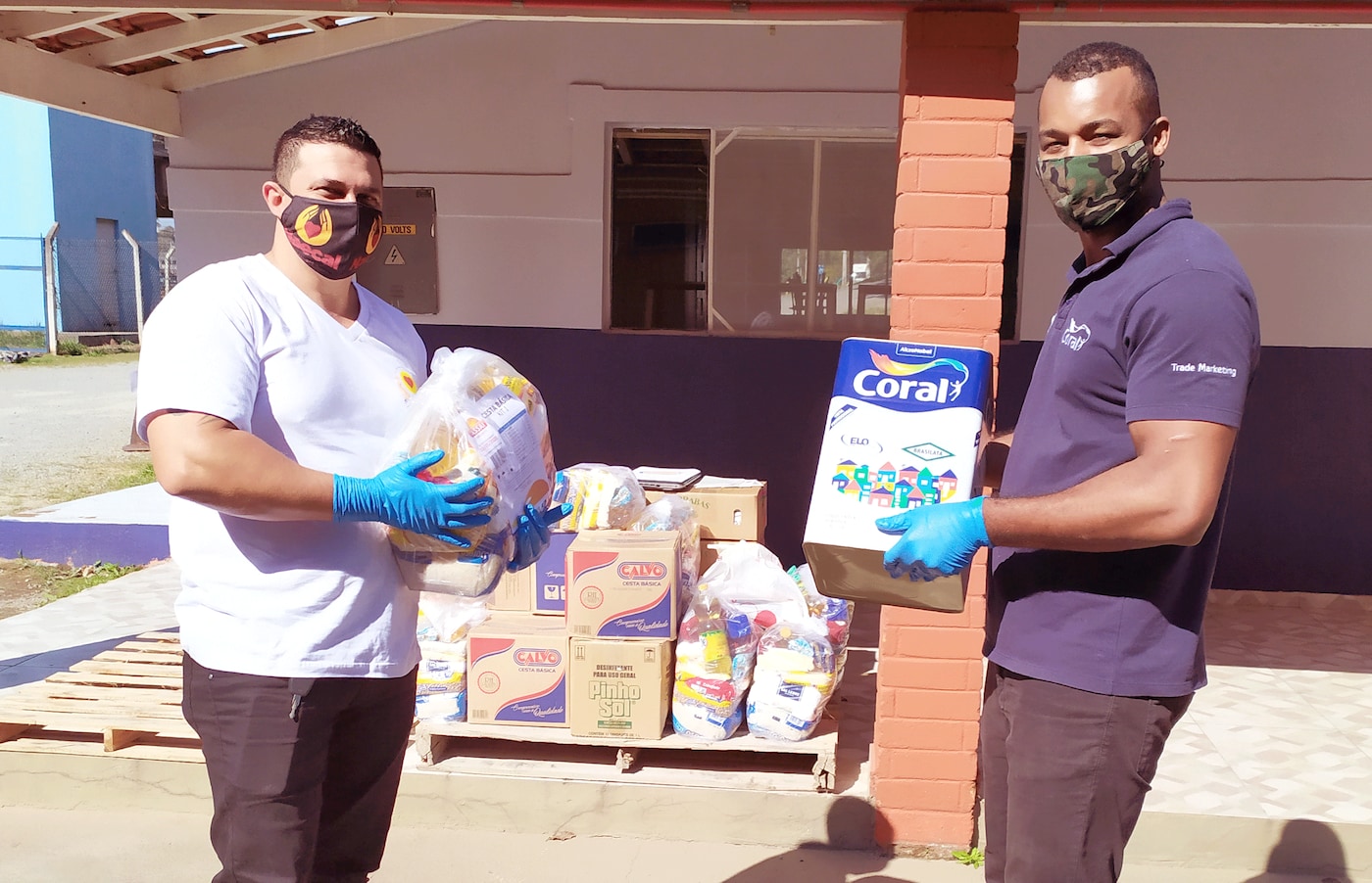 Dois homens segurando a arrecadação de alimentos e a lata de tintas Coral.