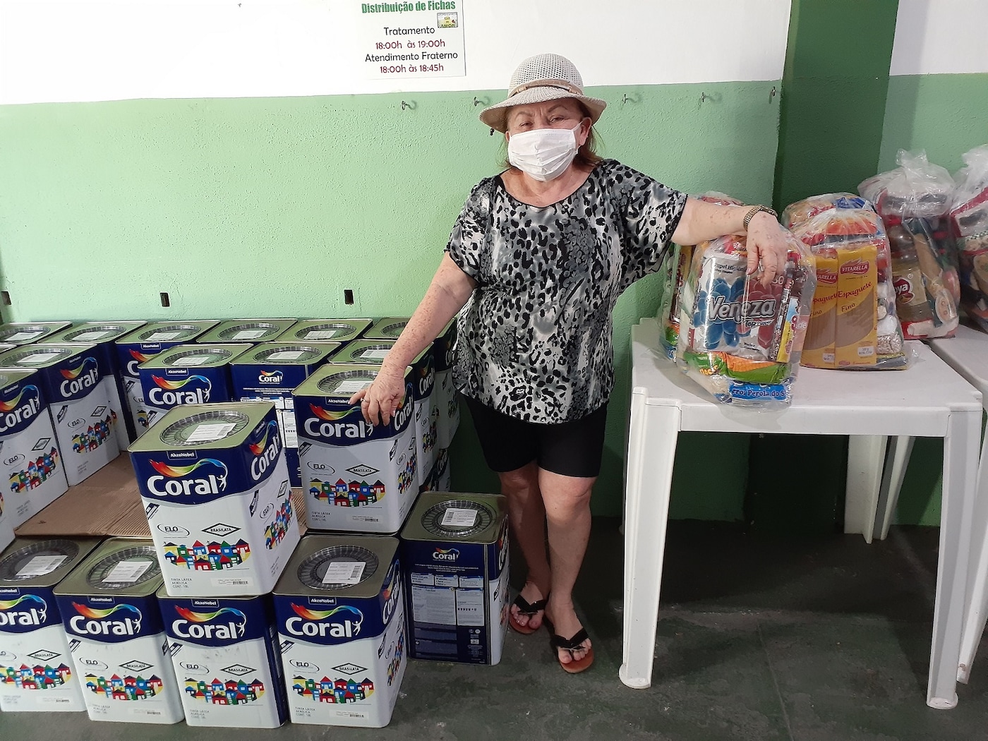 Mulher recebendo em mãos as arrecadações de alimentos em parceria com as Tintas Coral.