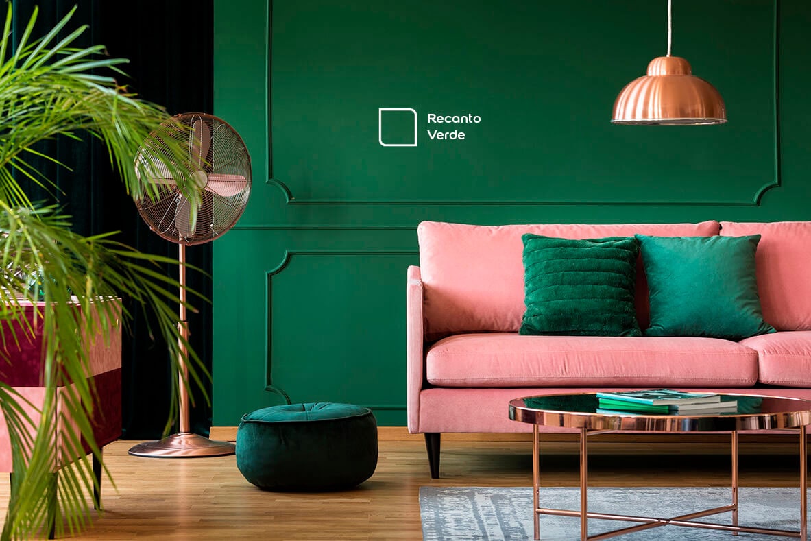 Sala de estar renovada com parede pintada na cor Verde Brasil da Tintas Coral. A cor verde da parede combina perfeitamente com o rosa do sofá, o ventilador vintage e os móveis, criando um ambiente delicado e aconchegante.