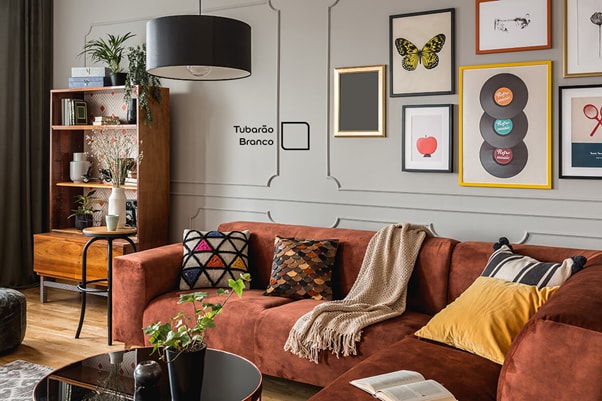 Sala de estar decorada com parede pintada na cor Tubarão Branco da Tintas Coral. Esse tom de neutro combinou perfeitamente com o sofá avermelhado e a decoração amarela do ambiente. 