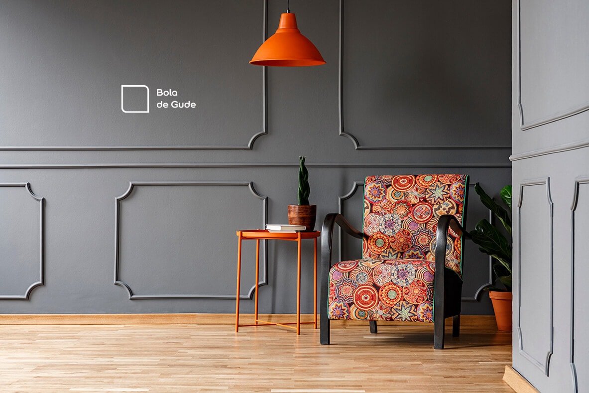 Ponto de destaque na sala criado em conjunto com a parede na cor Bola de Gude, um cinza muito clássico da Tintas Coral, que super combinou com a poltrona colorida em tons de laranja.