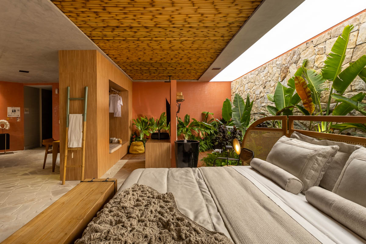 Os arquitetos falam muito sobre a importância de criar volumes nos ambientes. O que isso significa? Olhando esse quarto, a gente entende: os volumes são, por exemplo, as linhas cruzadas das prateleiras, os brises na cabeceira, e a moldura colorida que envolve a parede da cama. Tudo isso traz movimento ao espaço. A escolha de tons ajuda a ressaltar essa volumetria. Aqui, um verde com bastante azul na composição, faz um balanço com o resto da paleta neutra quente - baseada em terrosos e rosas. 