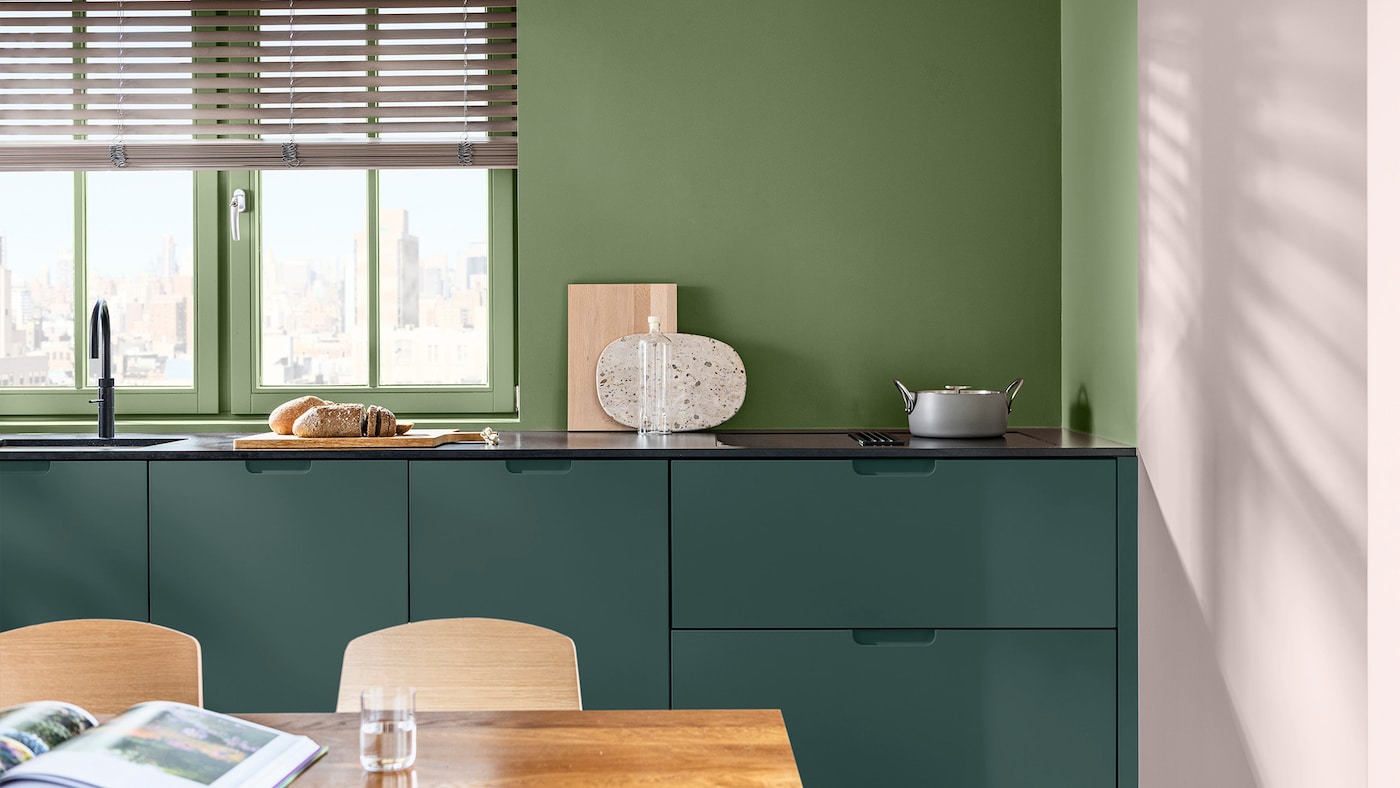 A kitchen with cabinets painted in forest green and walls above the kitchen cabinets painted in a lighter, brighter green. The adjacent wall is painted in soft pink. 