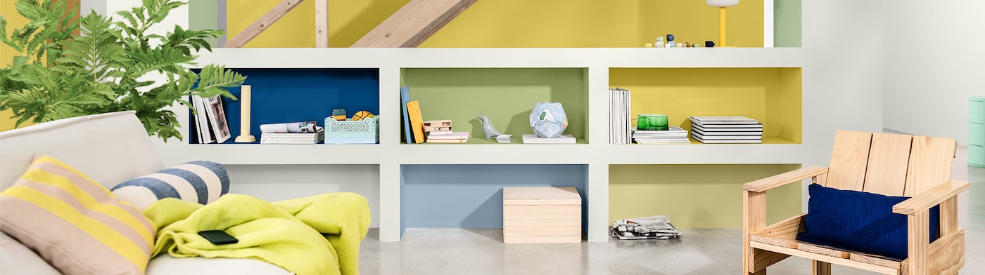 Dzīvojamā istaba ar dzeltenām sienām un baltiem un daudzkrāsainiem plauktiem 