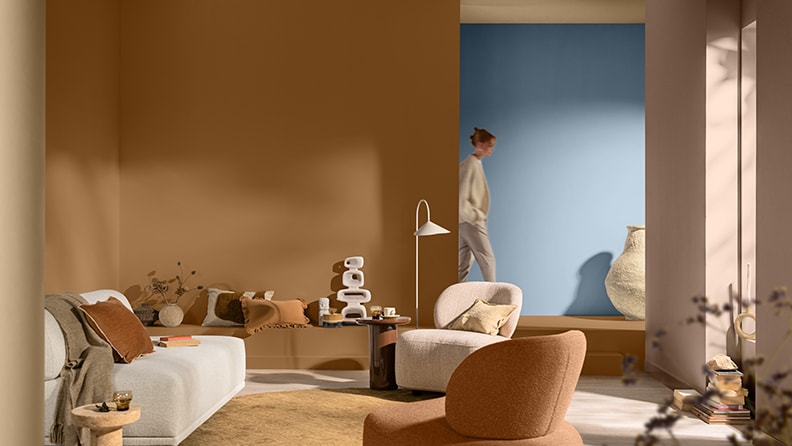 On the left there are painted balls in the back of a canvas with objects from around the world. On the right brown coloured wall with white sofa with boy walking in the living room