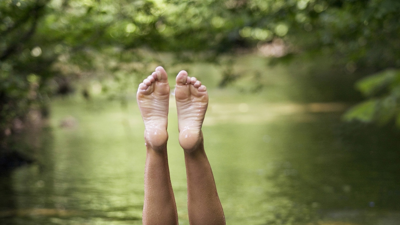 A woman performs a handstand in a lake that’s surrounded by lush lime green foliage.  