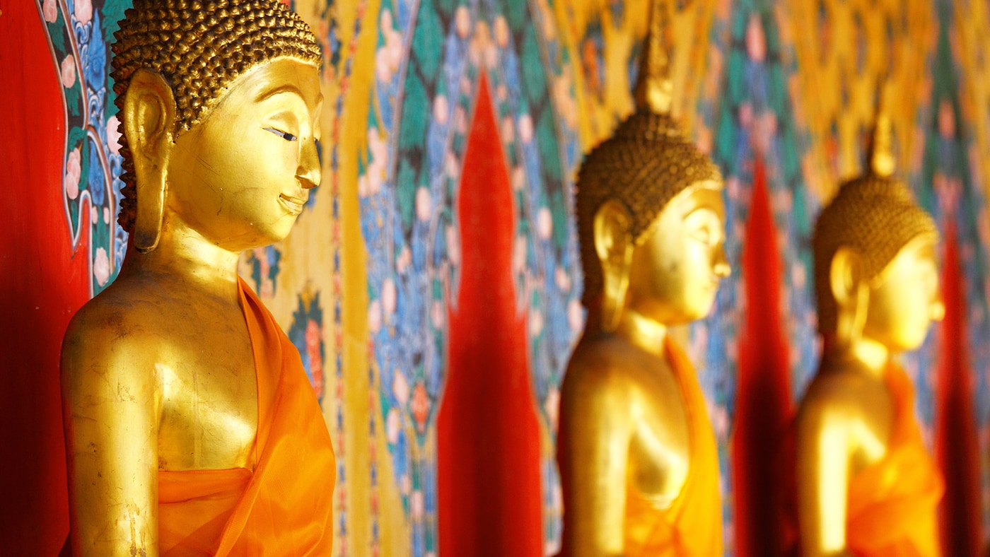 Gold Buddha statues sit against beautiful gold, red and blue material.