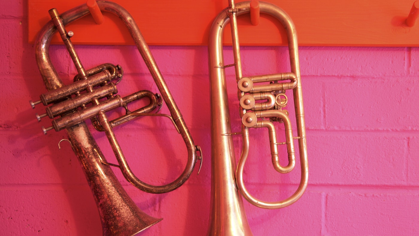 Gold trumpets against a bright pink and tangerine brick wall.