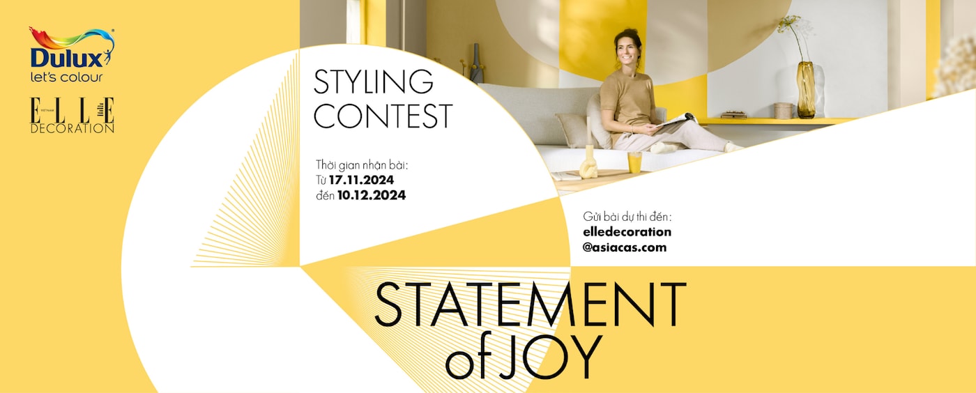 Người phụ nữ ngồi đọc khách trong không gian phòng khách, phía sau là mảng tường màu vàng được sơn họa tiết