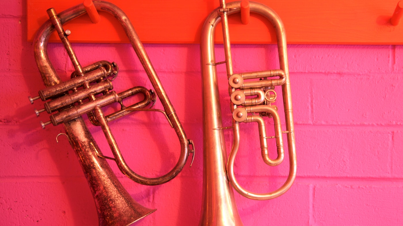 Gold trumpets against a bright pink and tangerine brick wall.