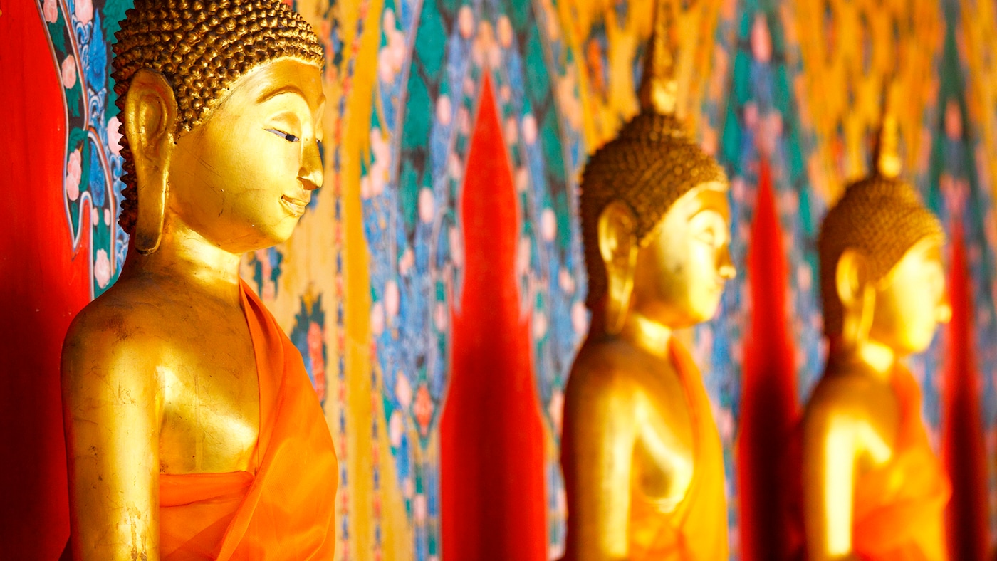 Gold Buddha statues sit against beautiful gold, red and blue material.