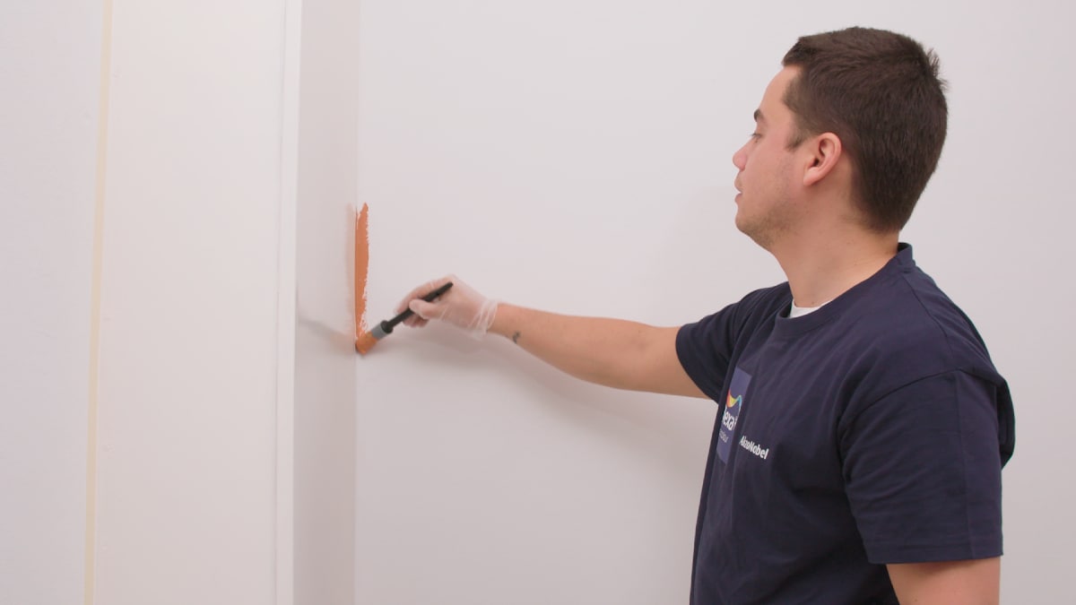 Wesley verft eerst de hoeken met een kwast met de kleur Binti Orient