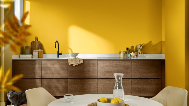 Een gele keuken met de houten keukenkastjes en de kleur True Joy op de muren