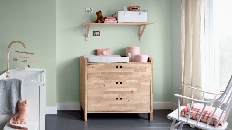 Een mintgroene babykamer met houten commode