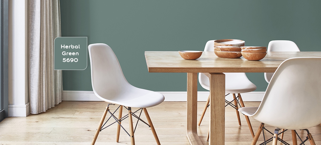 houten eettafel en witte stoelen in een kamer met een een groene muur