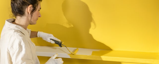 O femeie vopsește galben un perete, cu savana culoarea anului 2025