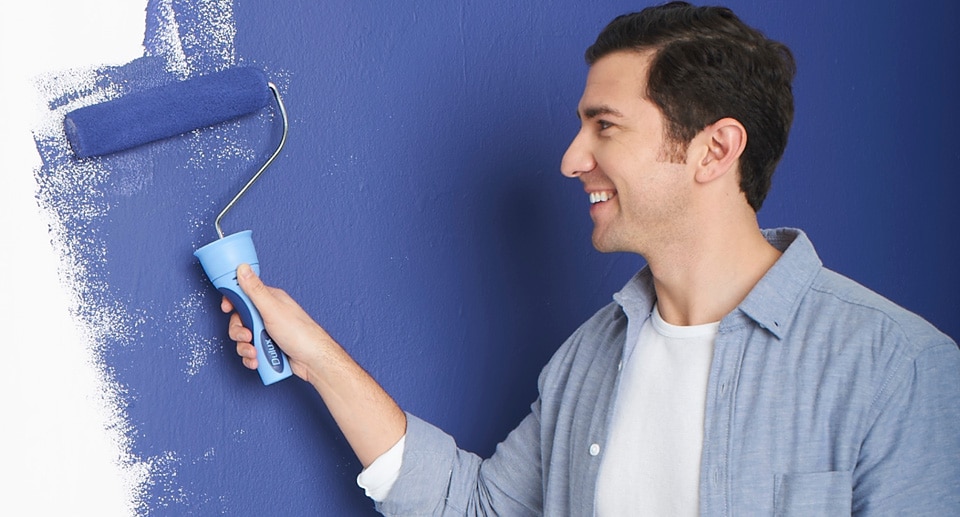 Νεαρός άντρας βάφει τοίχο με ρολό σε μπλε χρώμα