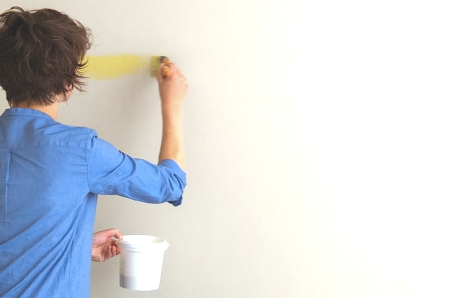 Γυναίκα βάφει τοίχο με πινέλο σε κίτρινη απόχρωση