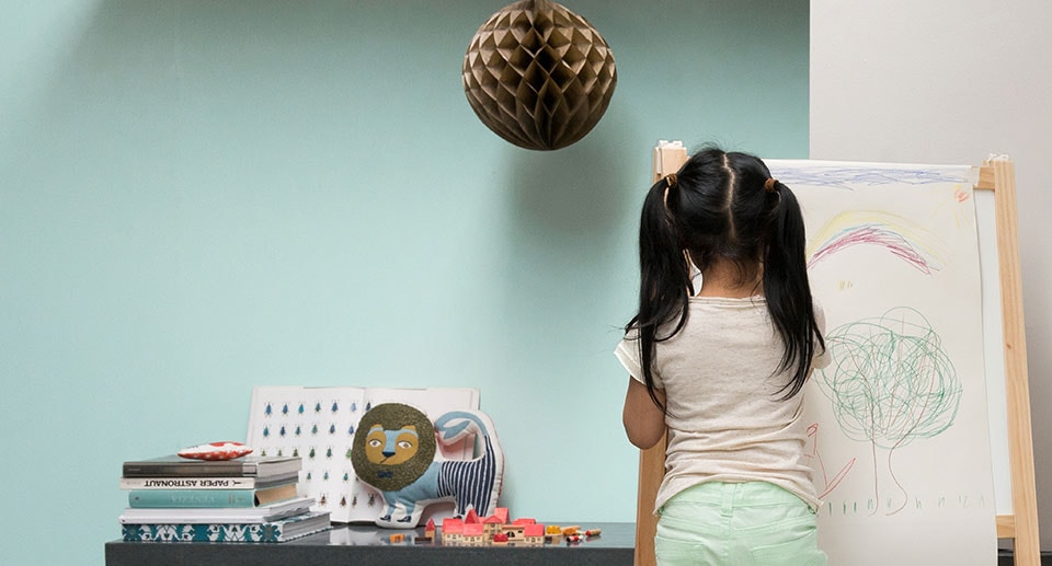 Γαλάζιος βεραμάν τοίχος σαλονιού μπροστά στον οποίο ένα κοριτσάκι ζωγραφίζει