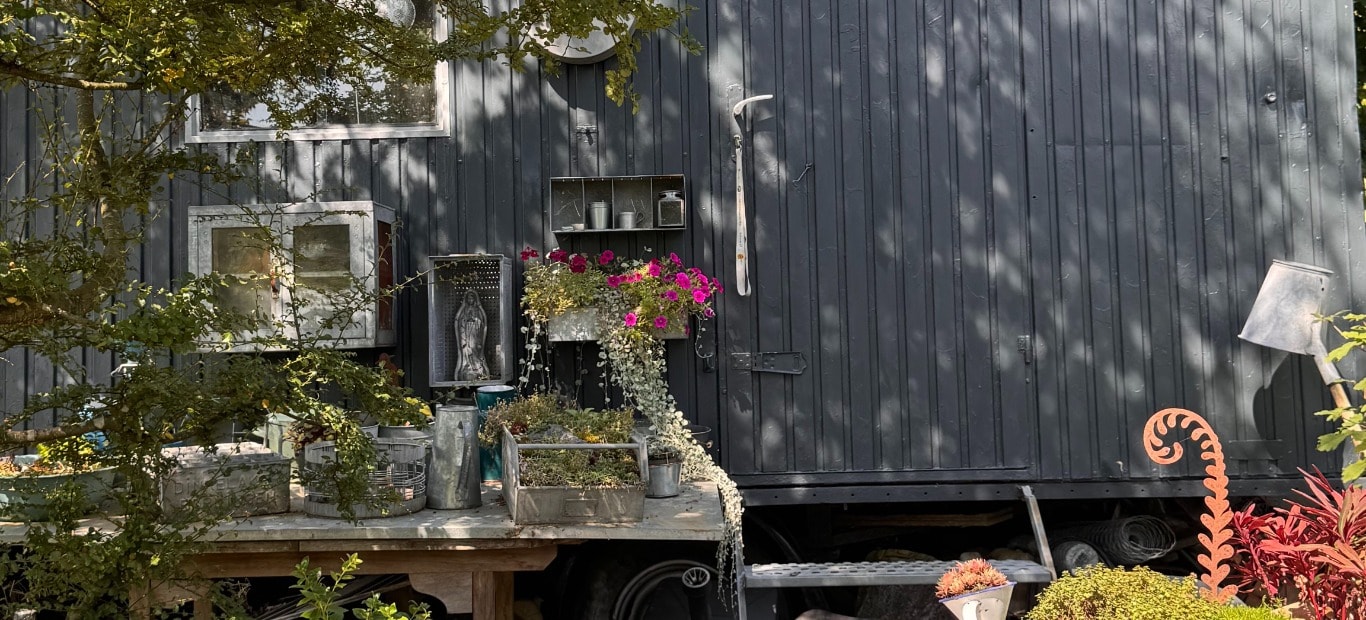 Ein mit Metallschutzlack von Hammerite gestrichener Bauwagen in Anthrazit, davor ein Tisch mit bepflanzten Dekoobjekten 
