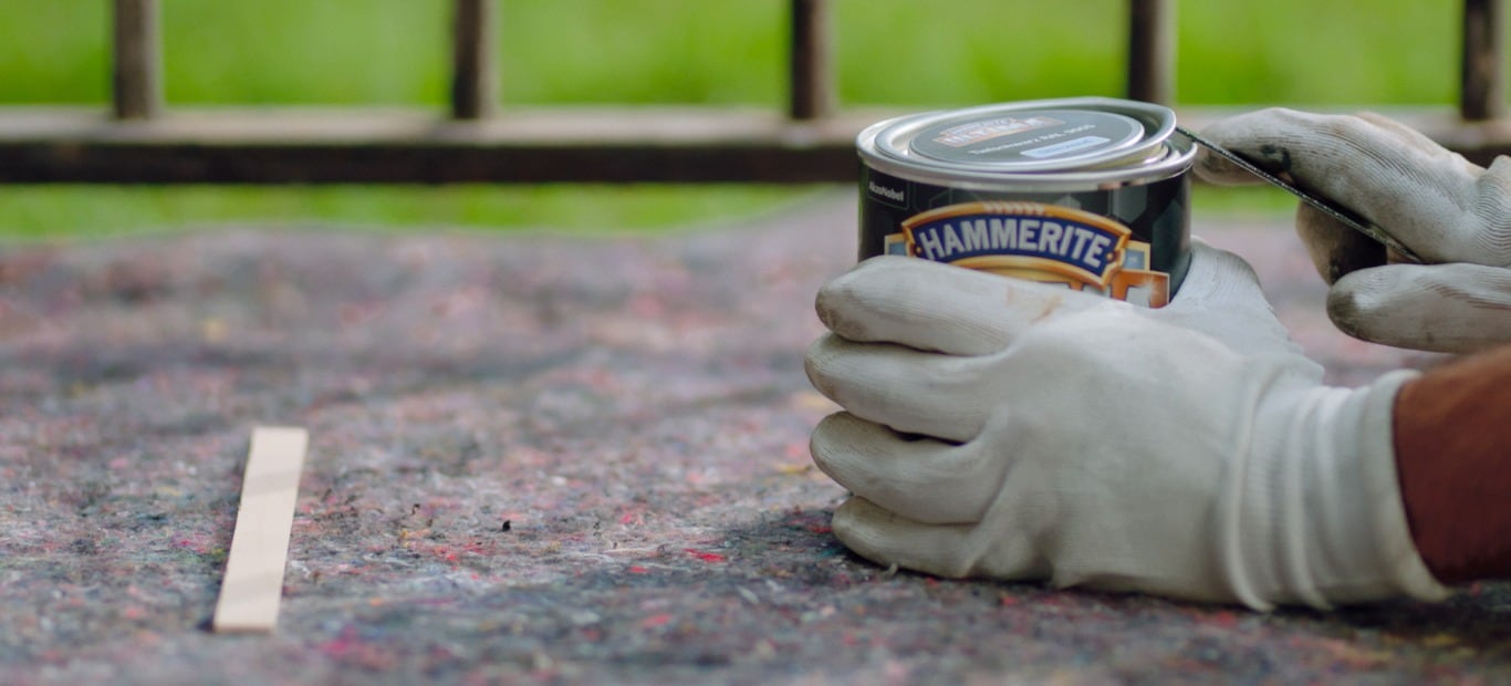 Eine Mann öffnet mit einem Lackdosenöffner eine Dose mit Metallschutzlack von Hammerite