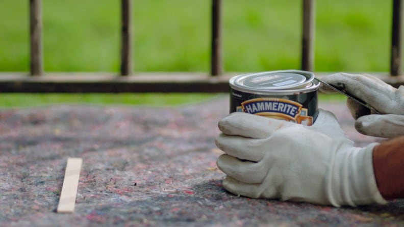 Eine Mann öffnet mit einem Lackdosenöffner eine Dose mit Metallschutzlack von Hammerite