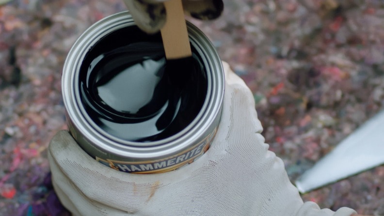 Jemand rührt mit einem Rührstab aus Holz Metallschutzlack von Hammerite in einer Dose um 