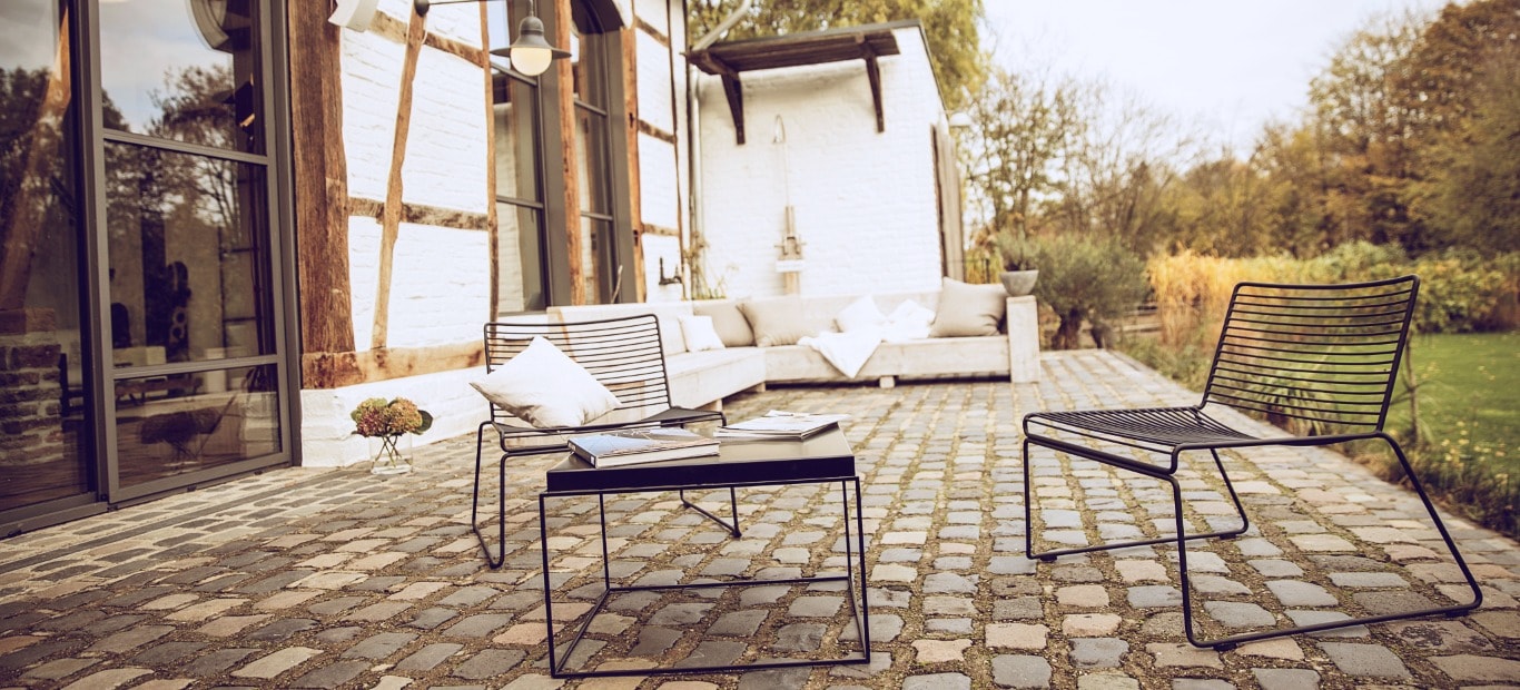 Gepflasterte Terrasse neben einem Fachwerkhaus mit Lounge und Sitzmöbeln aus Metall