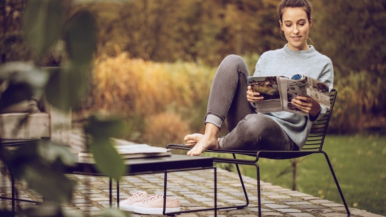 Eine Frau sitzt auf einer Terrasse in einem Metallstuhl und liest in einer Zeitschrift