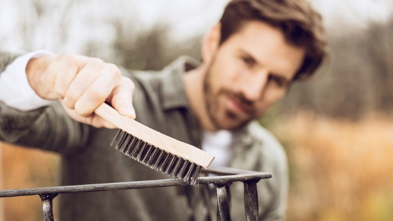 Ein Mann entfernt mit einer Drahtbürste lose sitzende Rostpartikel und alte Farbe von einem Balkongeländer