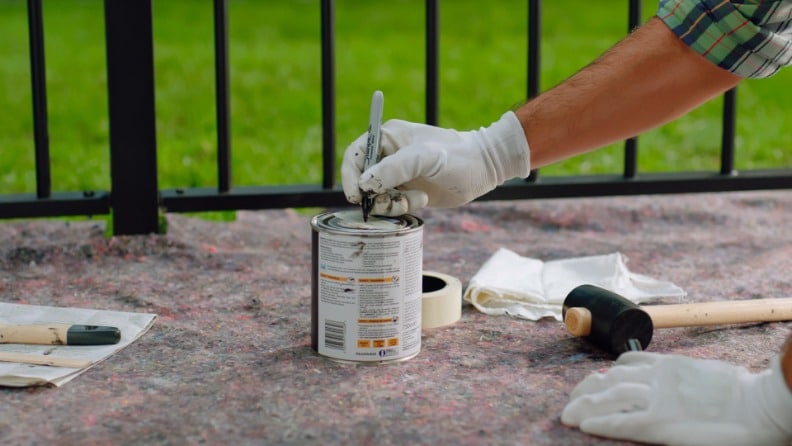 Ein Mann schreibt mit einem Edding das Öffnungsdatum auf eine Dose mit Metallschutzlack vor dem Lagern. 