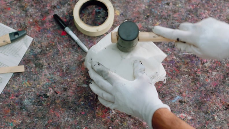 Ein Mann klopft mit einem Gummihammer den Deckel einer Dose mit Metallschutzlack fest, bevor er sie lagert. 