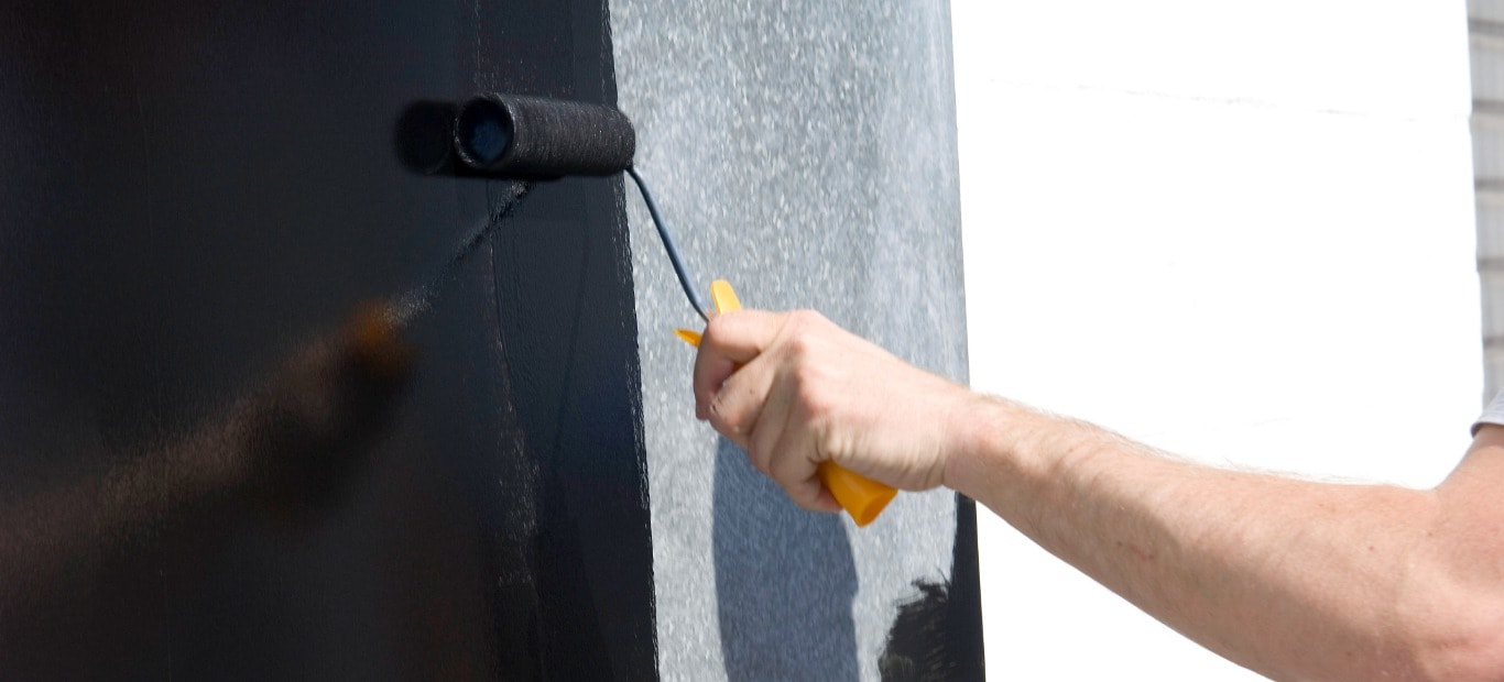Eine Metalltür wird mit einer Farbrolle schwarz gestrichen