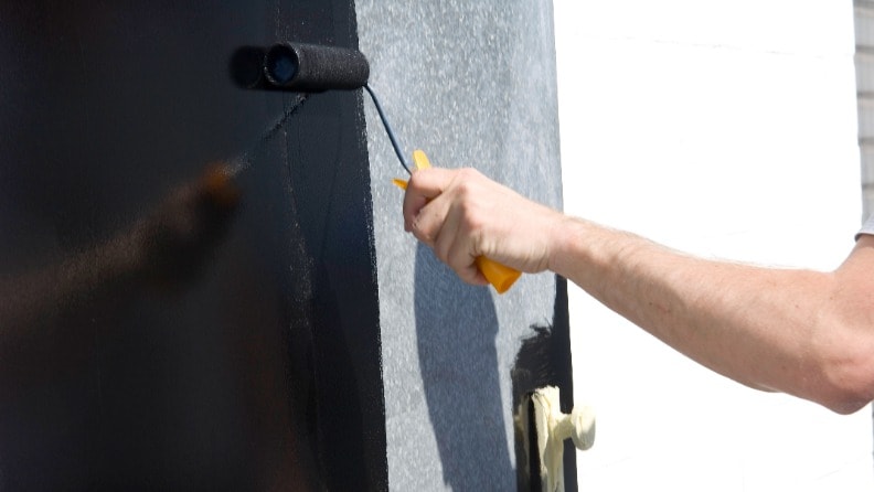 Eine Metalltür wird mit einer Farbrolle schwarz gestrichen