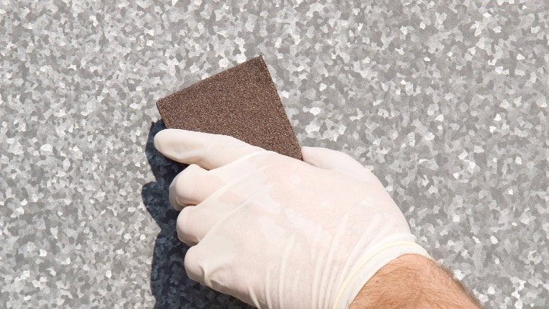 Eine Metalltür wird mit einem Schleifschwamm vor der Lackierung angeschliffen