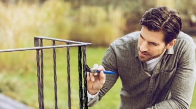 Ein Mann streicht ein Geländer mit dem Metall-Schutzlack Ultima von Hammerite