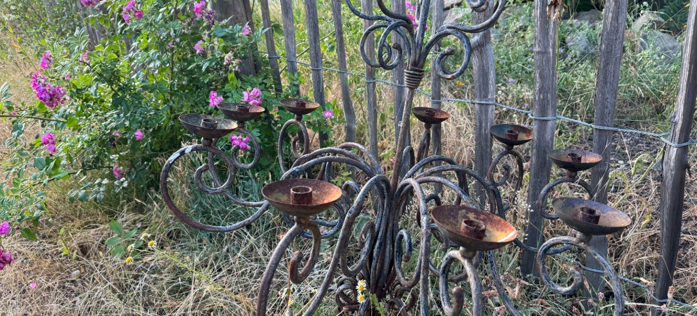 Ein verrosteter Kronleuchter steht angelehnt an einen Zaun im Garten vor der Behandlung mit einem Rostumwandler