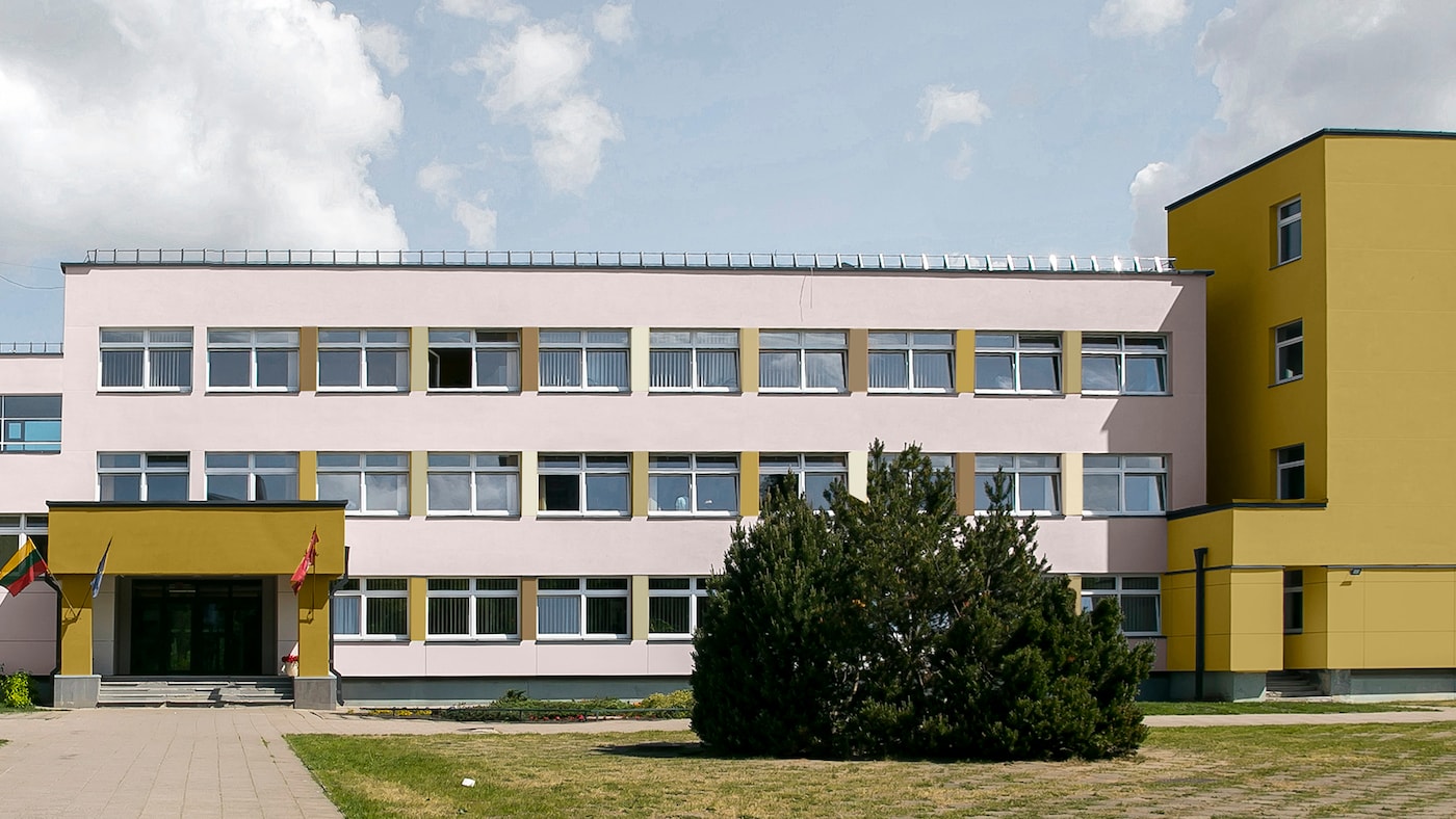 En skolebygning med ydervægge malet i en blød lyserød farve med accenter malet i okker 