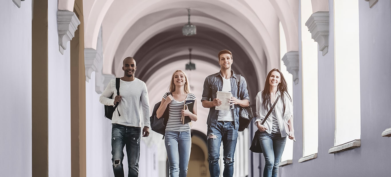 Fire studerende går gennem en gang med vægge malet i en blød lilla farve.