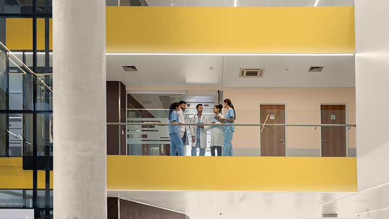 Læger og sygeplejersker taler sammen i en hospitalsbygning med gulmalede etageniveauer