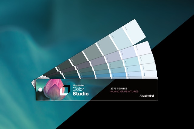 Nuancier de couleurs AkzoNobel Color Studio en forme d'éventail présentant des teintes de gris et bleus avec marquage "2079 teintes nuancier peintures" sur fond turquoise.
