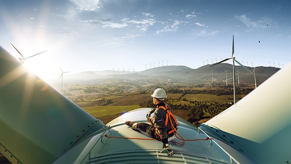 Un technicien équipé de matériel de sécurité est assis au sommet d'une éolienne, contemplant un paysage rempli d'éoliennes, symbole des efforts d’AkzoNobel en matière d'énergie durable.