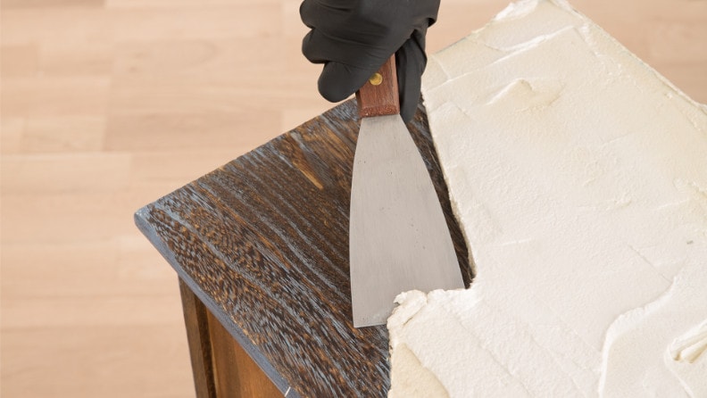 Alte Farbschichten werden mit einem Spachtel von einem Möbelstück abgetragen