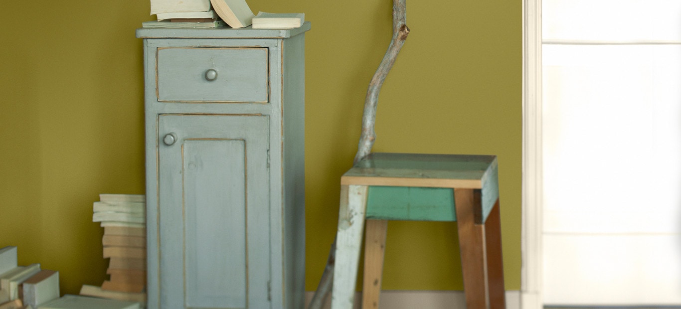 Upgecycelter Schrank und Hocker vor eine schlammgrünen Wand