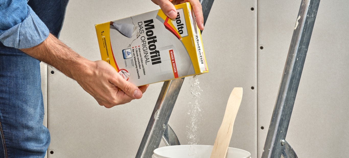 Mann rührt Spachtelmasse Moltofill - Das Original in einem Eimer an