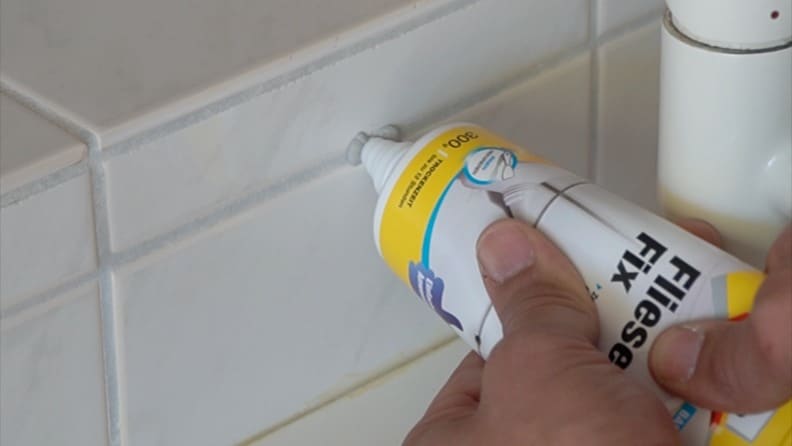Spachtelmasse wird direkt aus einer Tube Molto Fliesen Fix in ein Bohrloch in einer Fliese gedrückt