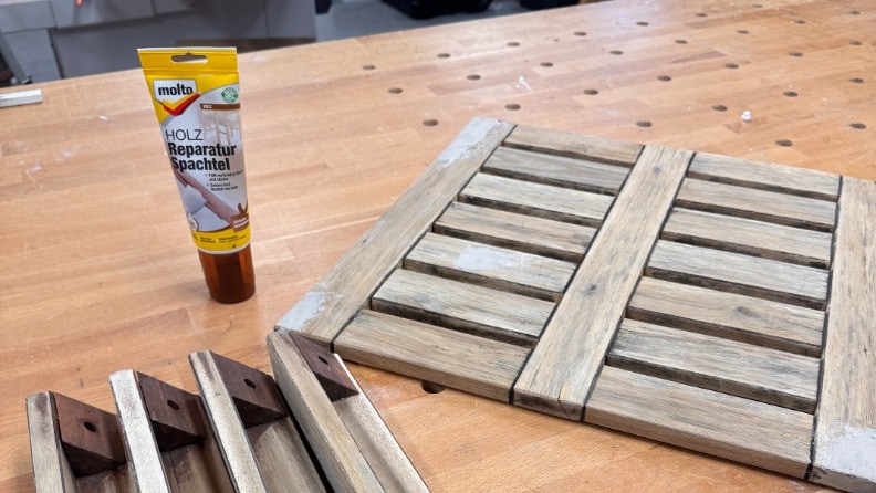 Eine Tube Molto Holz Reperatur Spachtel steht vor einem auseinandergebauten Holzhocker